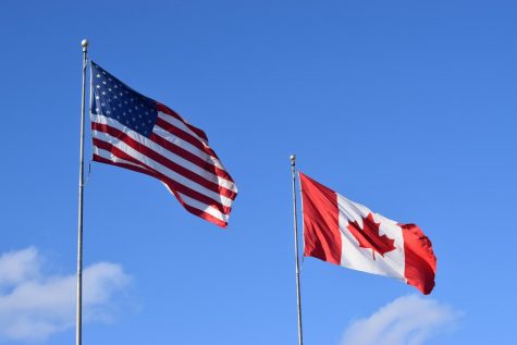 A Canadian and an American flag waving through the cold spring wind. At the Border between the two neighboring nations. 