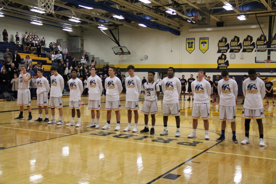 The boys basketball team stand side by side in silence during the national anthem before playing the Reds of Port Huron on January 16th, 2018